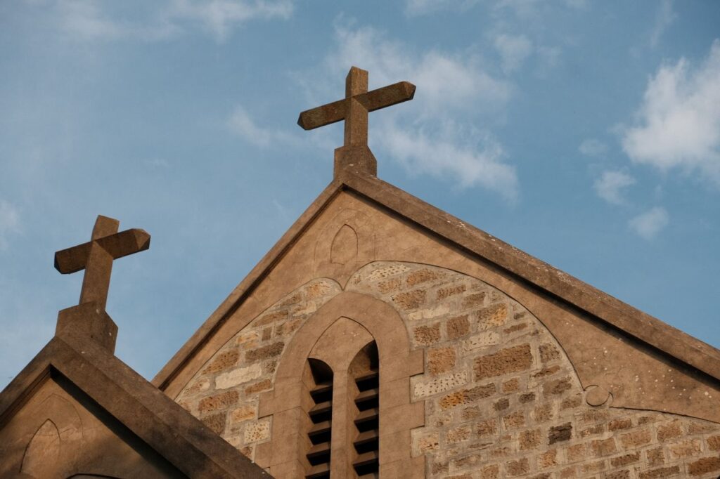 Low-angle view of a church facade with crosses against a bright blue sky.